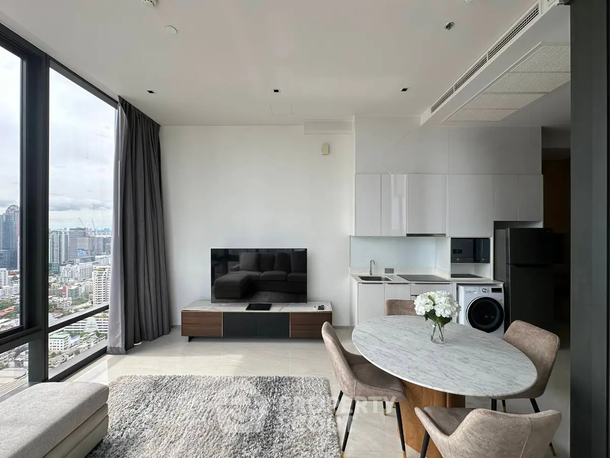 Modern living room with city view, featuring sleek furniture and open kitchen layout.