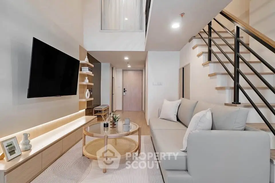 Modern living room with sleek design, featuring a cozy sofa, stylish staircase, and wall-mounted TV.