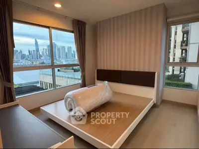 Modern bedroom with city skyline view and large windows in a high-rise apartment.