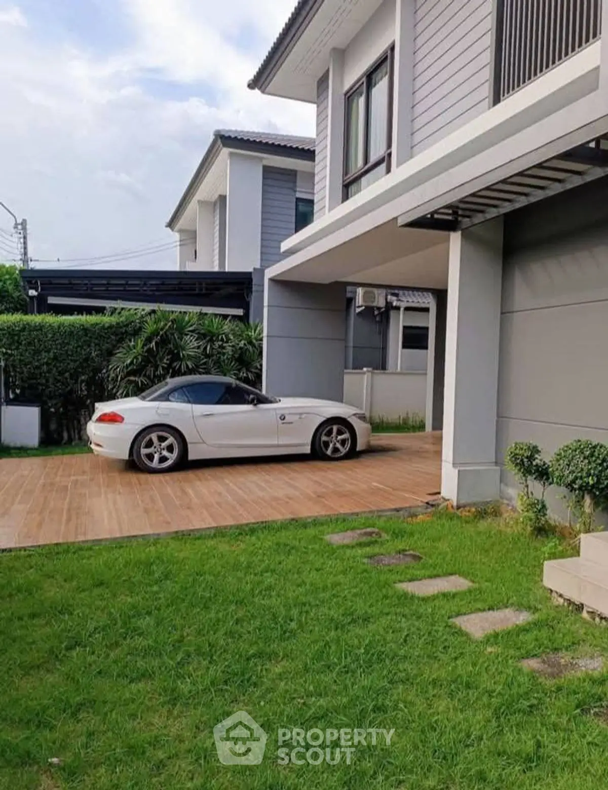 Modern suburban home with sleek car parked in driveway, lush green lawn, and contemporary architecture.