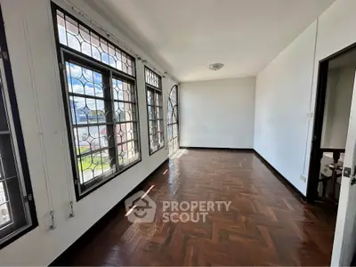 Spacious room with large windows and parquet flooring in a bright, airy space.