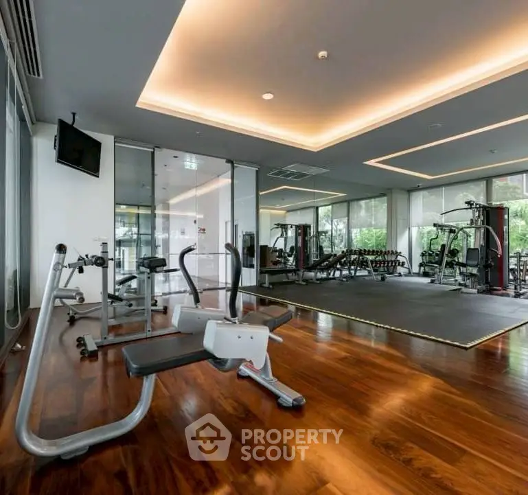 Luxurious gym with modern equipment and wooden flooring in upscale residential building.