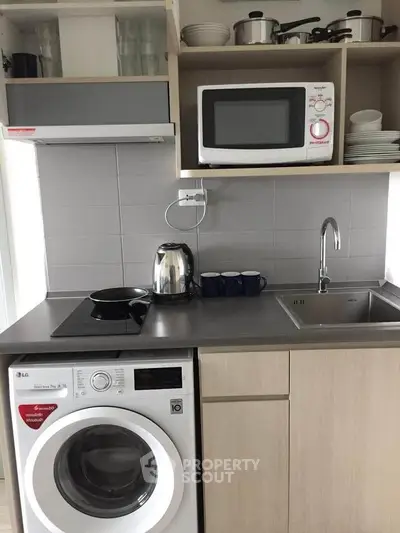 Modern compact kitchen with washing machine, microwave, and sleek cabinetry.