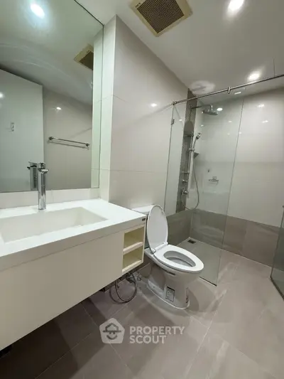 Modern bathroom with glass shower and sleek fixtures in contemporary apartment.