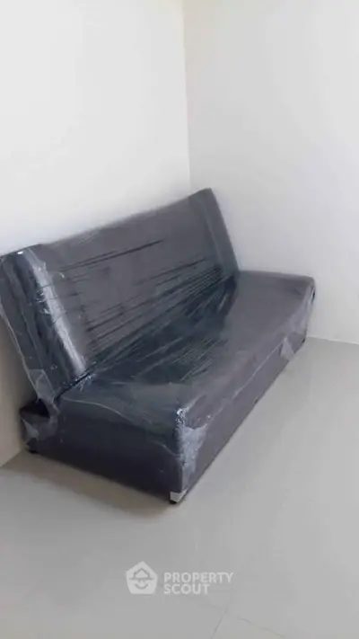 Minimalist room with a sleek black sofa wrapped in protective plastic, showcasing modern simplicity.