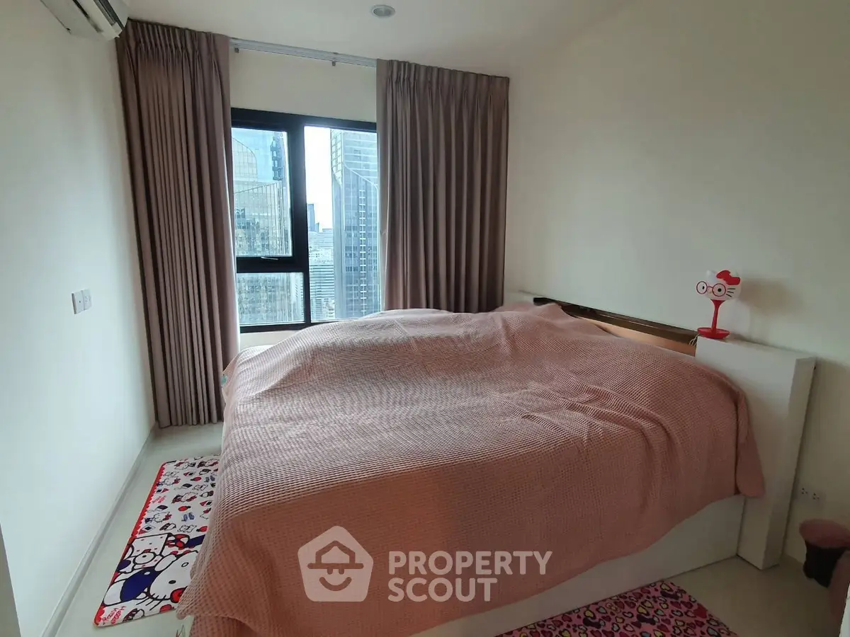 Cozy bedroom with city view, featuring large window and stylish decor.