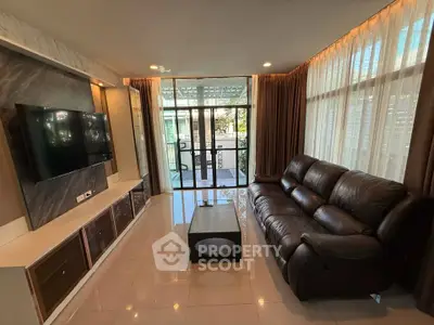 Modern living room with leather sofa and wall-mounted TV, featuring large windows and garden view.