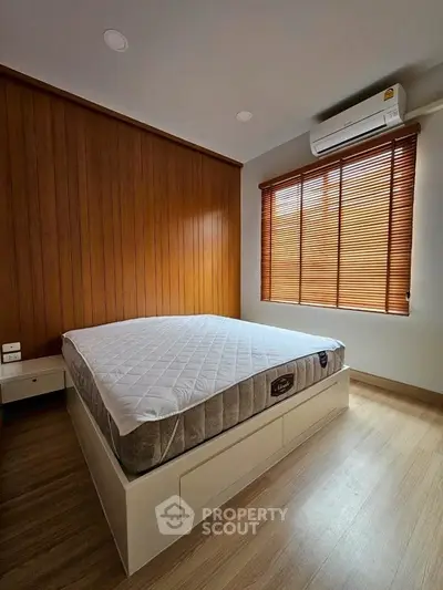 Cozy bedroom with wooden accents and natural light, featuring a comfortable bed and air conditioning.