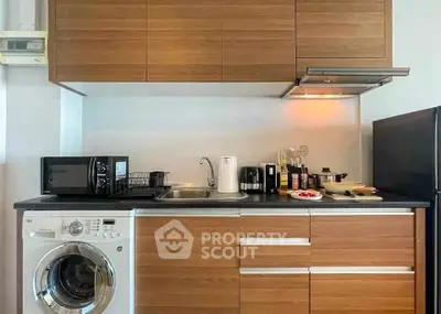 Modern kitchen with wooden cabinets, washing machine, and sleek appliances in a compact layout.