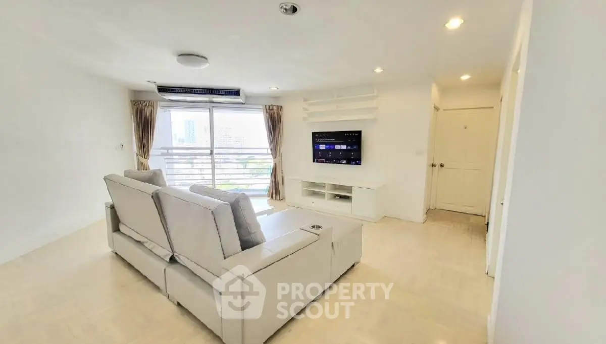 Spacious modern living room with large windows and city view, featuring a comfortable sofa and wall-mounted TV.
