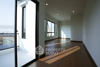 Spacious modern living room with large windows and balcony access, featuring sleek wooden flooring.