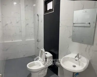 Modern bathroom with sleek fixtures and marble tiles, featuring a toilet, sink, and shower area.