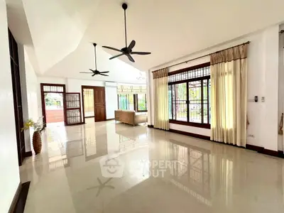 Spacious living room with large windows and ceiling fans, offering abundant natural light.