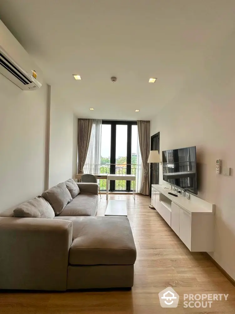 Modern living room with large sofa and TV, featuring floor-to-ceiling windows and wooden flooring.