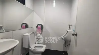 Modern bathroom with toilet, urinal, and sink in sleek white tiles.