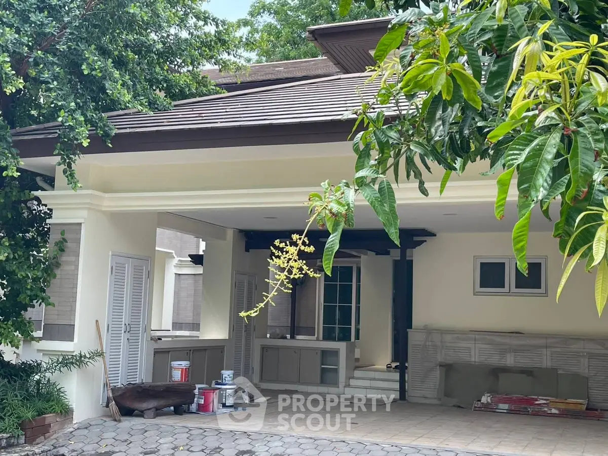 Charming residential entrance with lush greenery and spacious driveway.