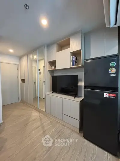 Modern living room with sleek storage and black fridge in stylish apartment.