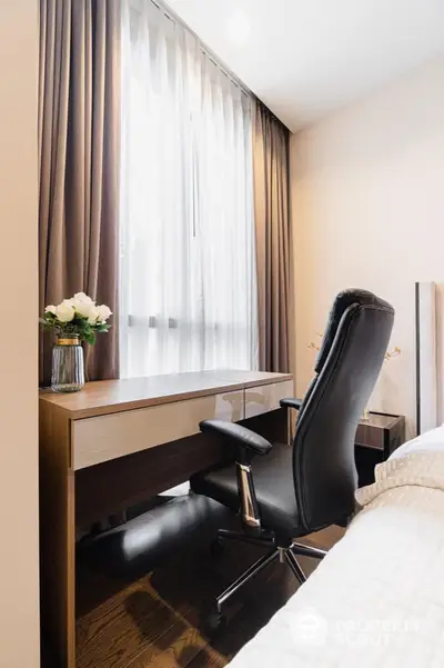 Elegant home office nook with a sleek wooden desk, comfortable black chair, and sheer curtains filtering natural light.