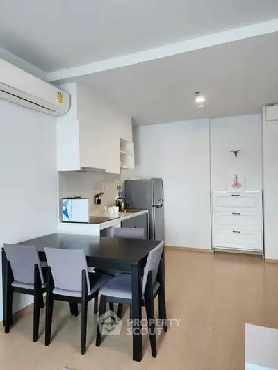 Modern dining area with sleek black table and chairs, adjacent to a compact kitchen with fridge.