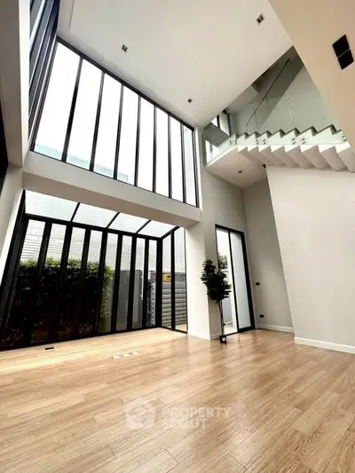 Spacious modern living room with high ceilings and large windows, offering abundant natural light and elegant wooden flooring.