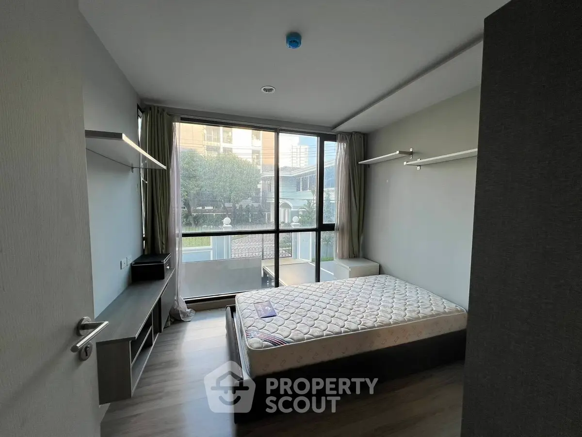 Spacious bedroom with large window and modern furnishings in a stylish apartment.