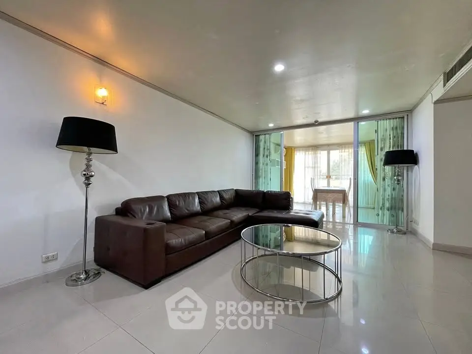 Spacious living room with modern leather sofa and glass coffee table, leading to a bright dining area.