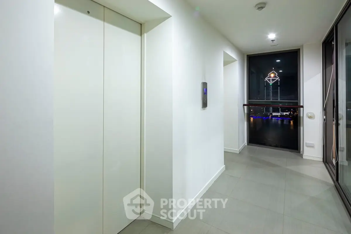 Modern apartment hallway with elevator and city view window at night.