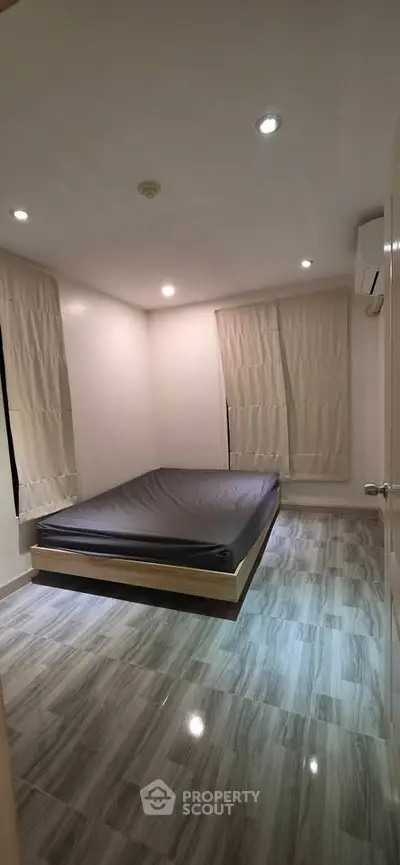 Spacious bedroom with modern flooring and minimalist design, featuring a comfortable bed and ample natural light.