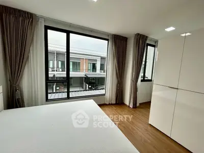 Modern bedroom with large windows and stylish curtains, offering a view of contemporary architecture.