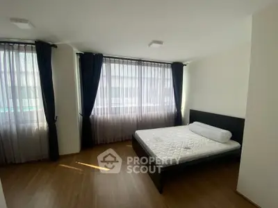 Spacious bedroom with large windows and modern furnishings in a bright apartment.