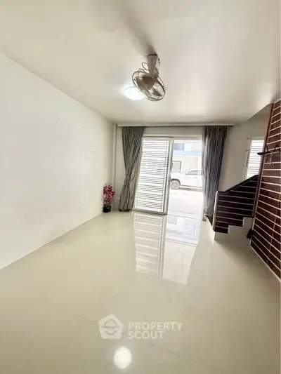 Spacious living room with large windows and modern staircase, perfect for natural light and open living.