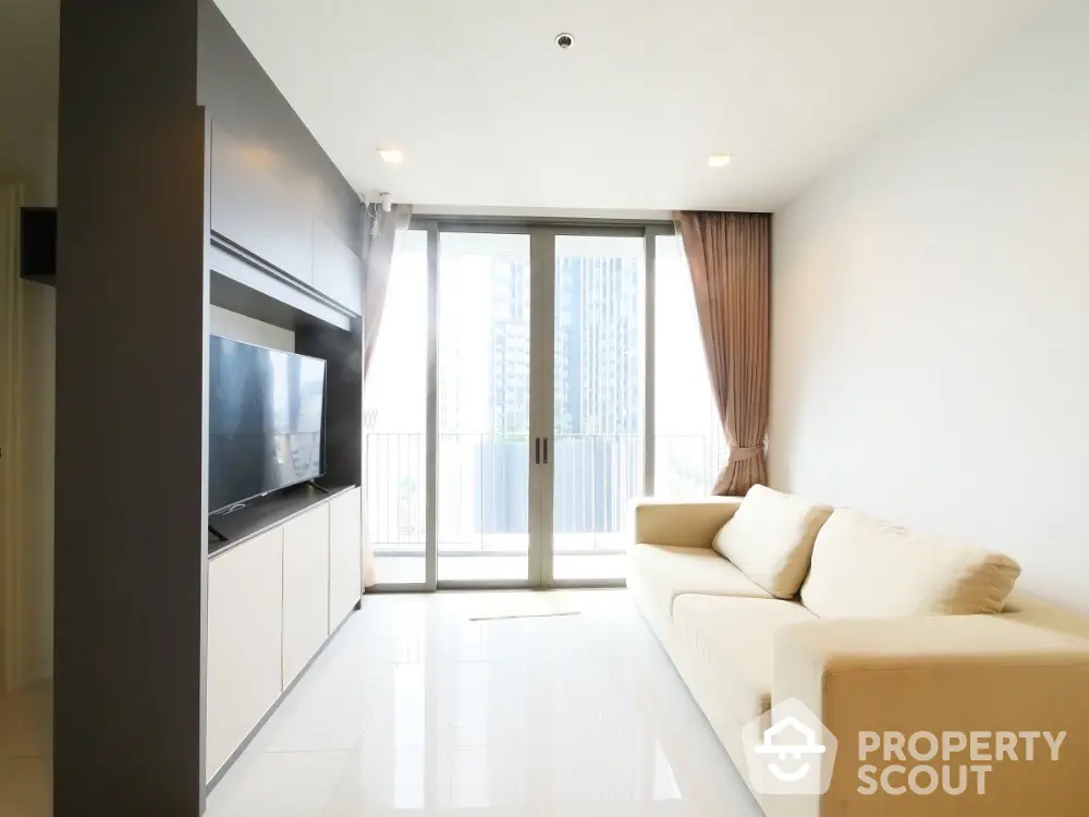 Modern living room with large windows and city view, featuring a cozy beige sofa and sleek TV unit.