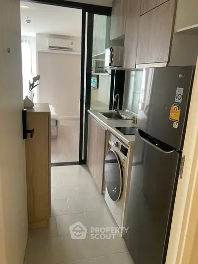 Modern compact kitchen with washing machine and fridge in stylish apartment.
