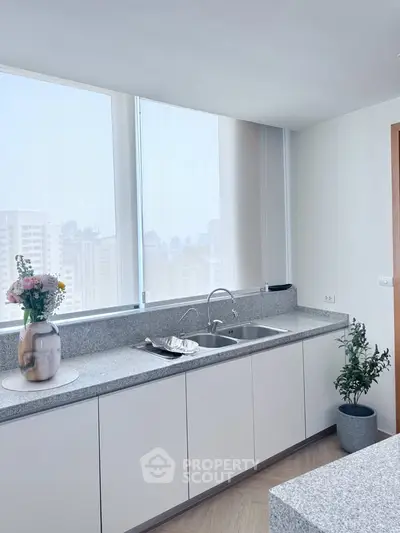 Modern kitchen with sleek countertops and city view, featuring elegant decor and ample natural light.