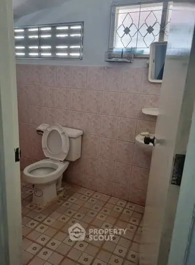 Cozy bathroom with pink tiled walls and floor, featuring a classic toilet and small window.