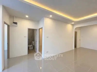 Spacious modern interior with sleek tile flooring and recessed lighting, featuring a bathroom entrance.