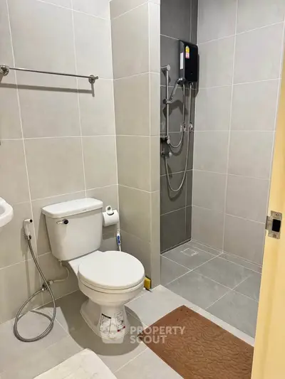 Modern bathroom with sleek tiles and shower area, featuring a toilet and bath mat.