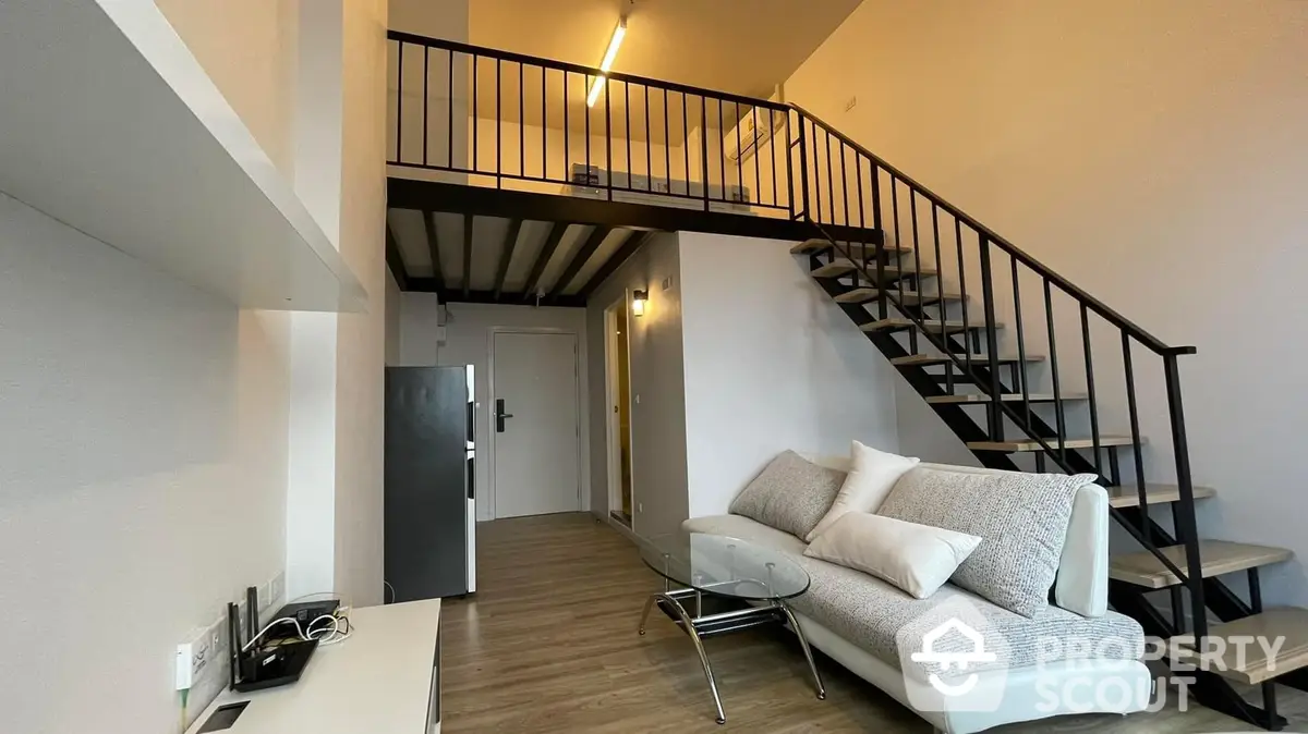 Spacious loft-style living room with high ceiling, modern sofa, and elegant staircase leading to an upper level, showcasing a contemporary urban living space.