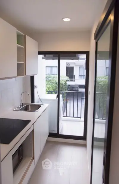 Modern kitchen with sleek design and balcony view, featuring built-in appliances and ample natural light.