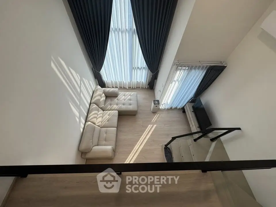 Spacious modern living room with high ceilings and elegant curtains, featuring a cozy white sofa and sleek TV setup.