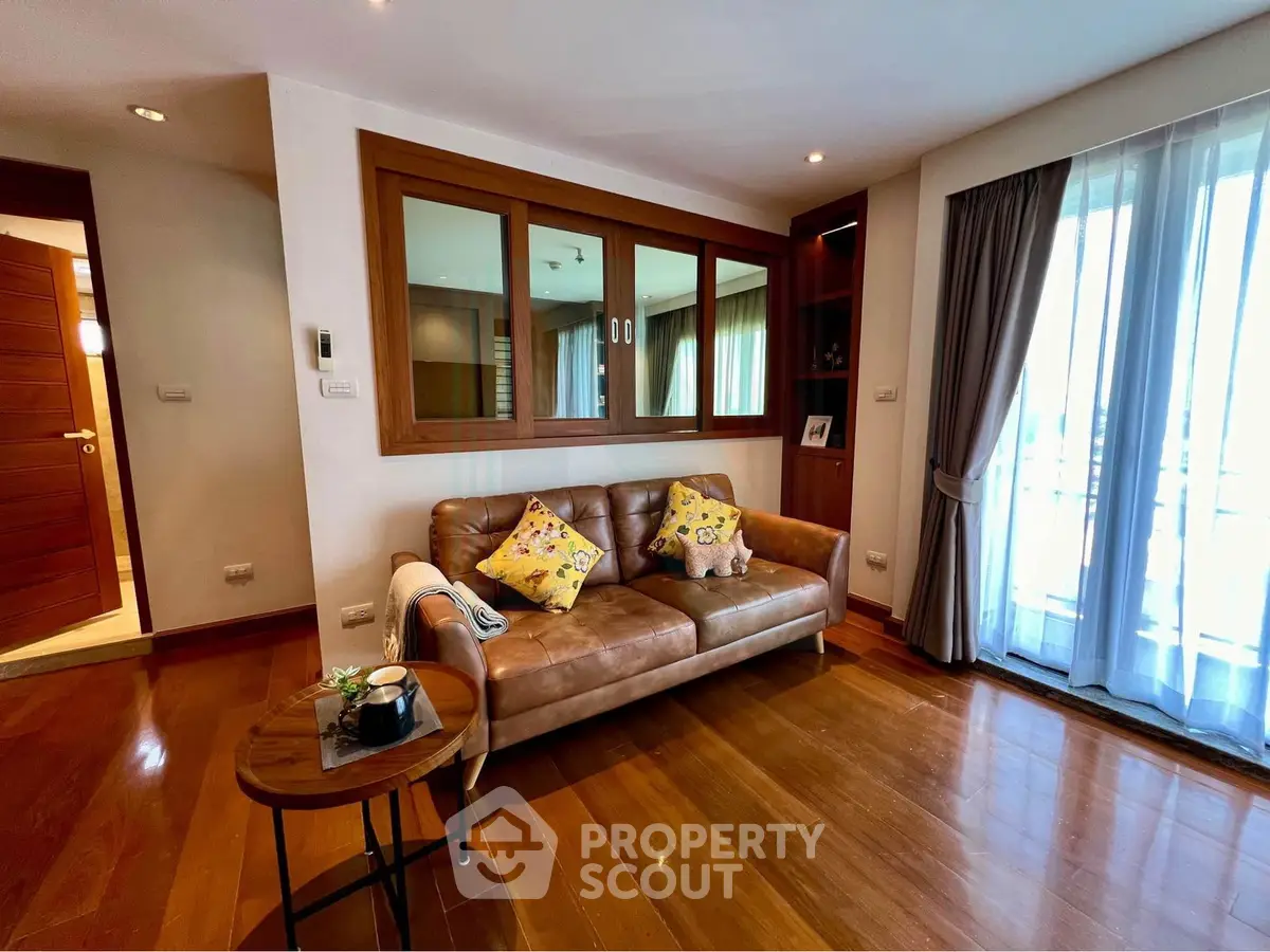 Charming living room with leather sofa and wooden flooring, featuring large windows for natural light.