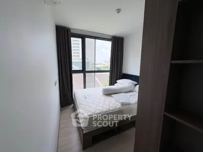 Cozy bedroom with large window and modern furnishings in a high-rise apartment.