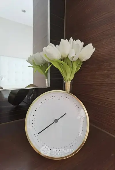 Elegant bedroom decor with modern clock and fresh tulips on wooden shelf.