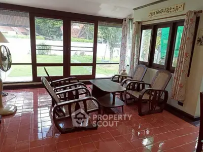 Charming living room with large windows and garden view, featuring elegant wooden furniture and tiled flooring.