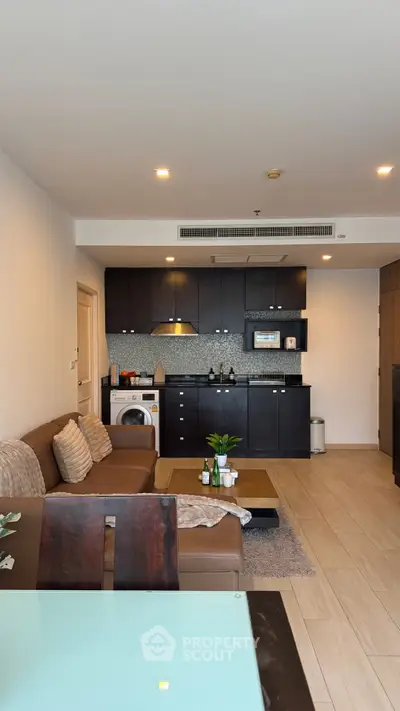 Modern living room with open kitchen, featuring sleek cabinetry and cozy seating area.