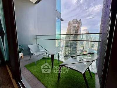 Modern balcony with city view, stylish chairs, and artificial grass flooring in high-rise apartment.