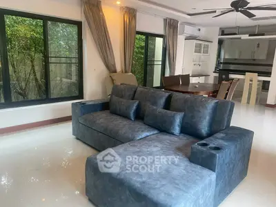 Spacious living room with modern sofa and large windows overlooking greenery.