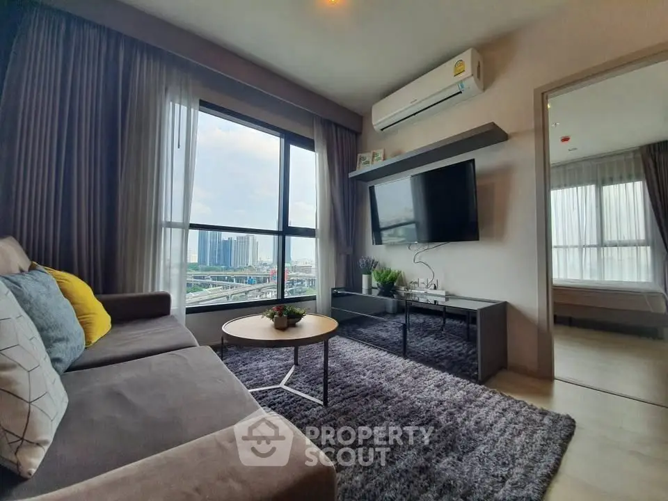 Modern living room with large windows and city view, featuring cozy sofa and wall-mounted TV.