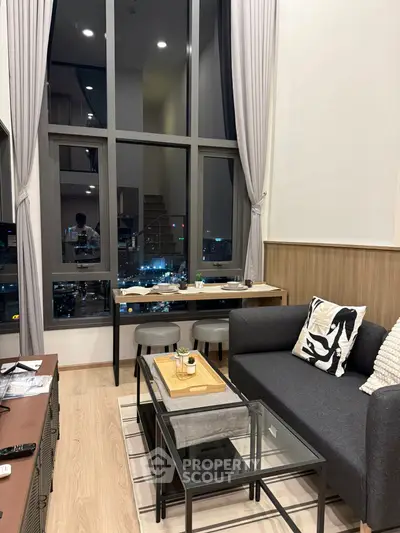 Modern living room with high ceilings and city view, featuring stylish furniture and large windows.