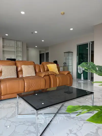 Spacious modern living room with leather sofa and glass coffee table, perfect for relaxation and entertaining.